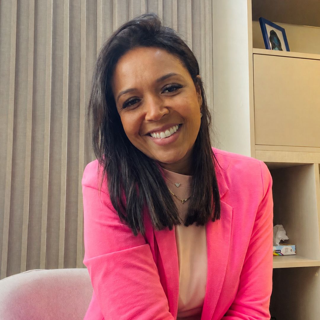 Patrícia Nascente sorrindo em seu consultório, vestindo blazer rosa